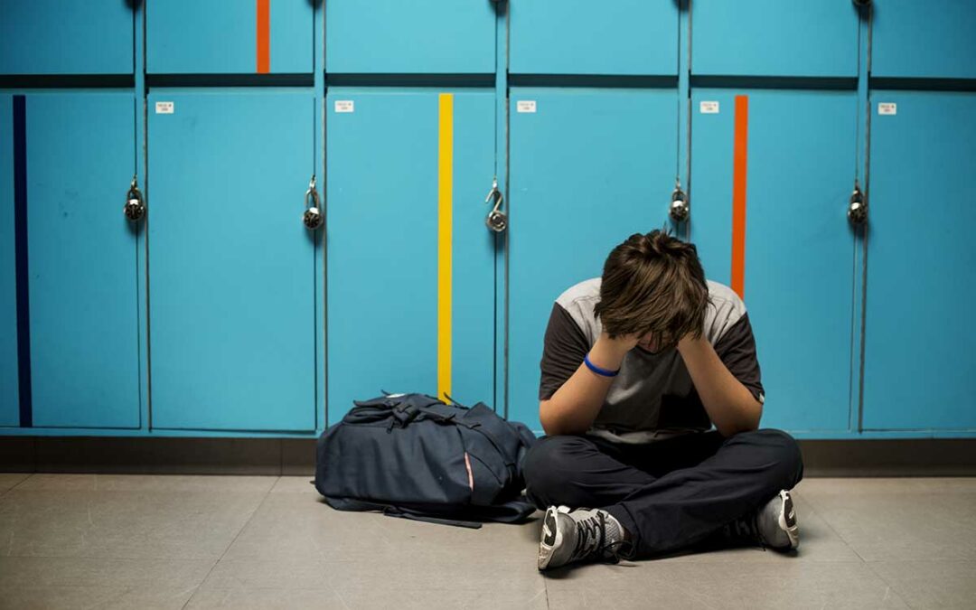 Child sitting on the ground, hands on face upset in a school hallway.