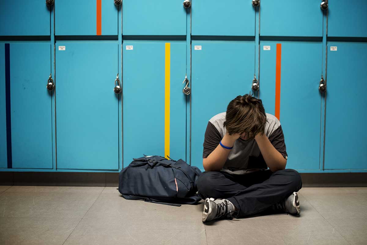 Child sitting on the ground, hands on face upset in a school hallway.