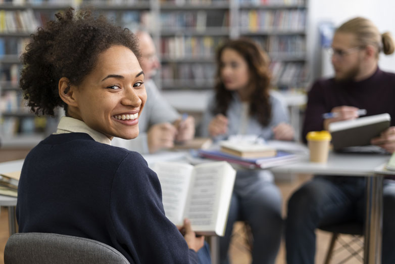 Person reading in a classroom and smiling at the camera Person reading in a classroom and smiling at the camera