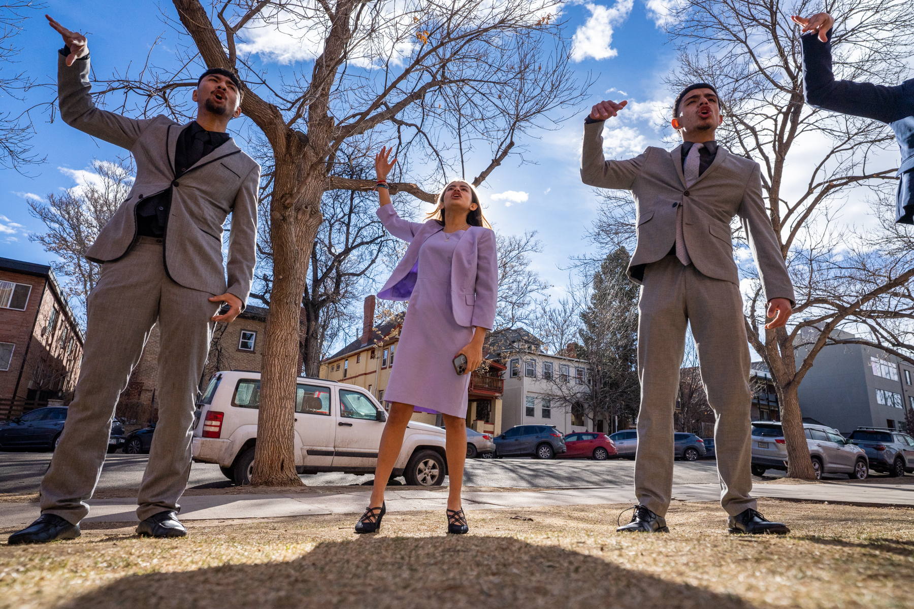 Three students standing outside, each with their right hand up.