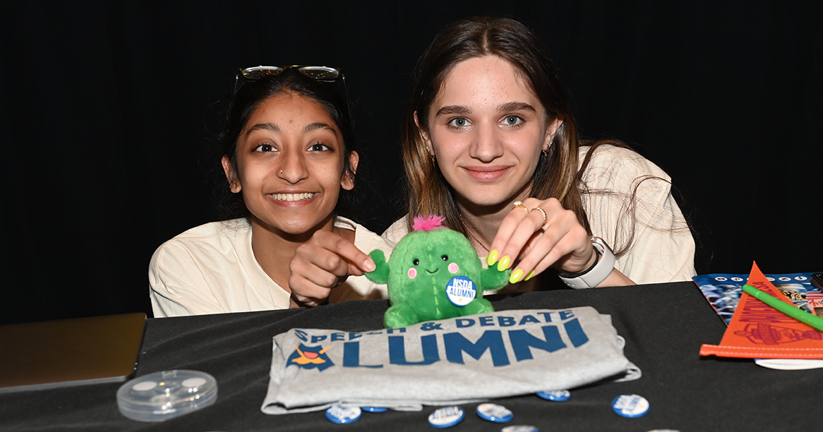 Two students with a cactus plushie and a speech and debate alumni t-shirt.