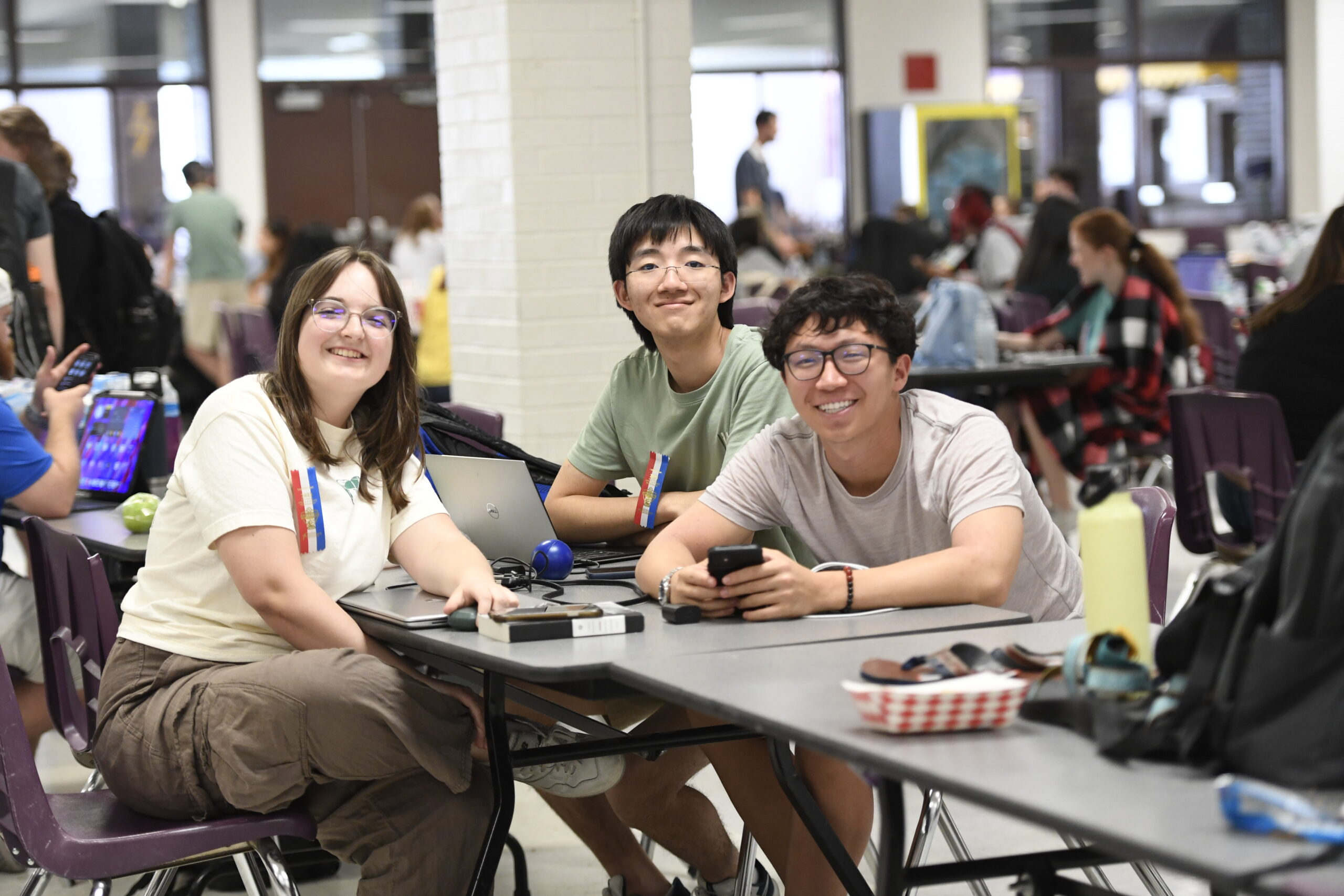 Three students smiling at the camera sitting in a large room