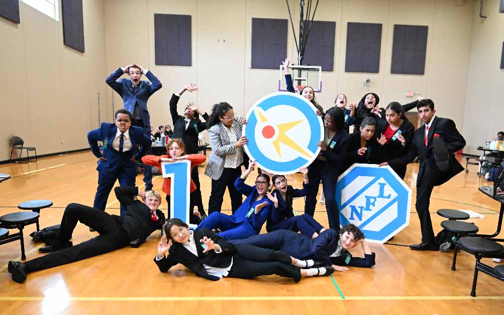Group of students posing with the National Speech & Debate Centennial logo in a gym