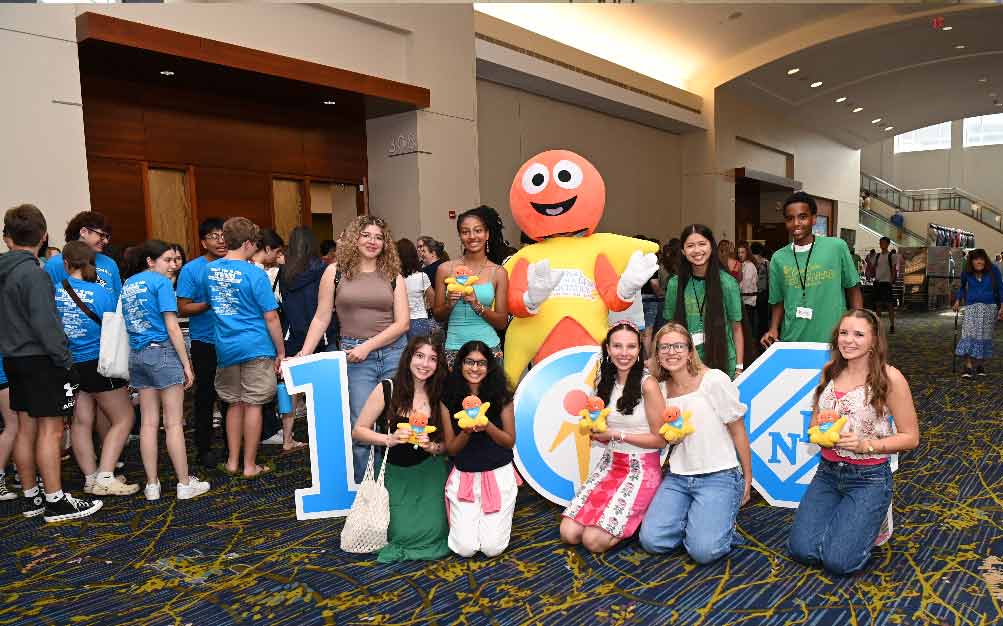 Group of people at Sunday registration posing with the NSDA mascot at the National Tournament