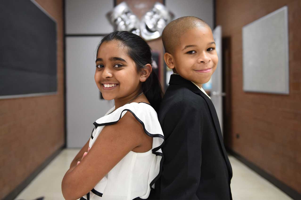 Two students standing back to back smiling