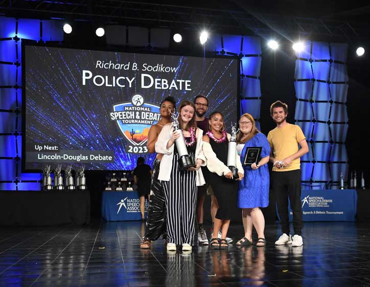 Group of students standing on stage at the National Tournament with their trophies Group of students standing on stage at the National Tournament with their trophies