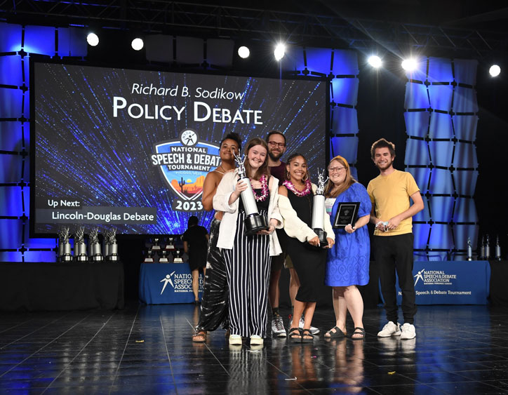 Group of students standing on stage at the National Tournament with their trophies