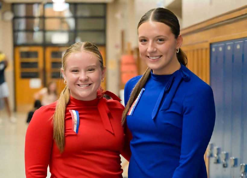 Two students in a hallway posing together smiling